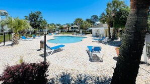 A pool area with lounge chairs and a small building, surrounded by trees and a clear sky. - Great 1 BDR Condo in the center of Myrtle Beach (Myrtle Beach)