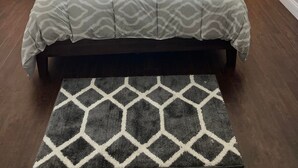 A bedroom with a bed, two bedside tables with lamps, a window with curtains, and a geometric rug. - Ranch home with 3 bedrooms upstairs and 1 down. Refurnished June of 2022 (St. Ignace)