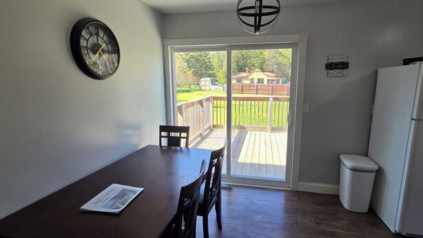 A kitchen with a refrigerator, a dining table with chairs, a clock on the wall, and a sliding glass door leading to a deck. - Ranch home with 3 bedrooms upstairs and 1 down. Refurnished June of 2022 (St. Ignace)