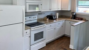 A kitchen with white cabinets, a microwave, a stove, a coffee maker, and a window. - Ranch home with 3 bedrooms upstairs and 1 down. Refurnished June of 2022 (St. Ignace)