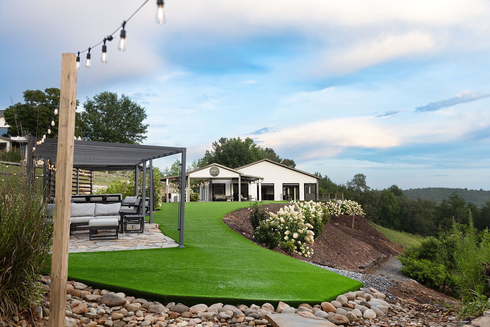 A modern house with a covered patio, a well-maintained lawn, and a view of the surrounding landscape.