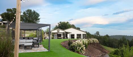 A modern house with a covered patio, a well-maintained lawn, and a view of the surrounding landscape.