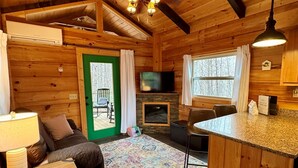 Ein gemütliches Blockhaus-Interieur mit Holzbalkendecke, Kamin, Fernseher und Essbereich.