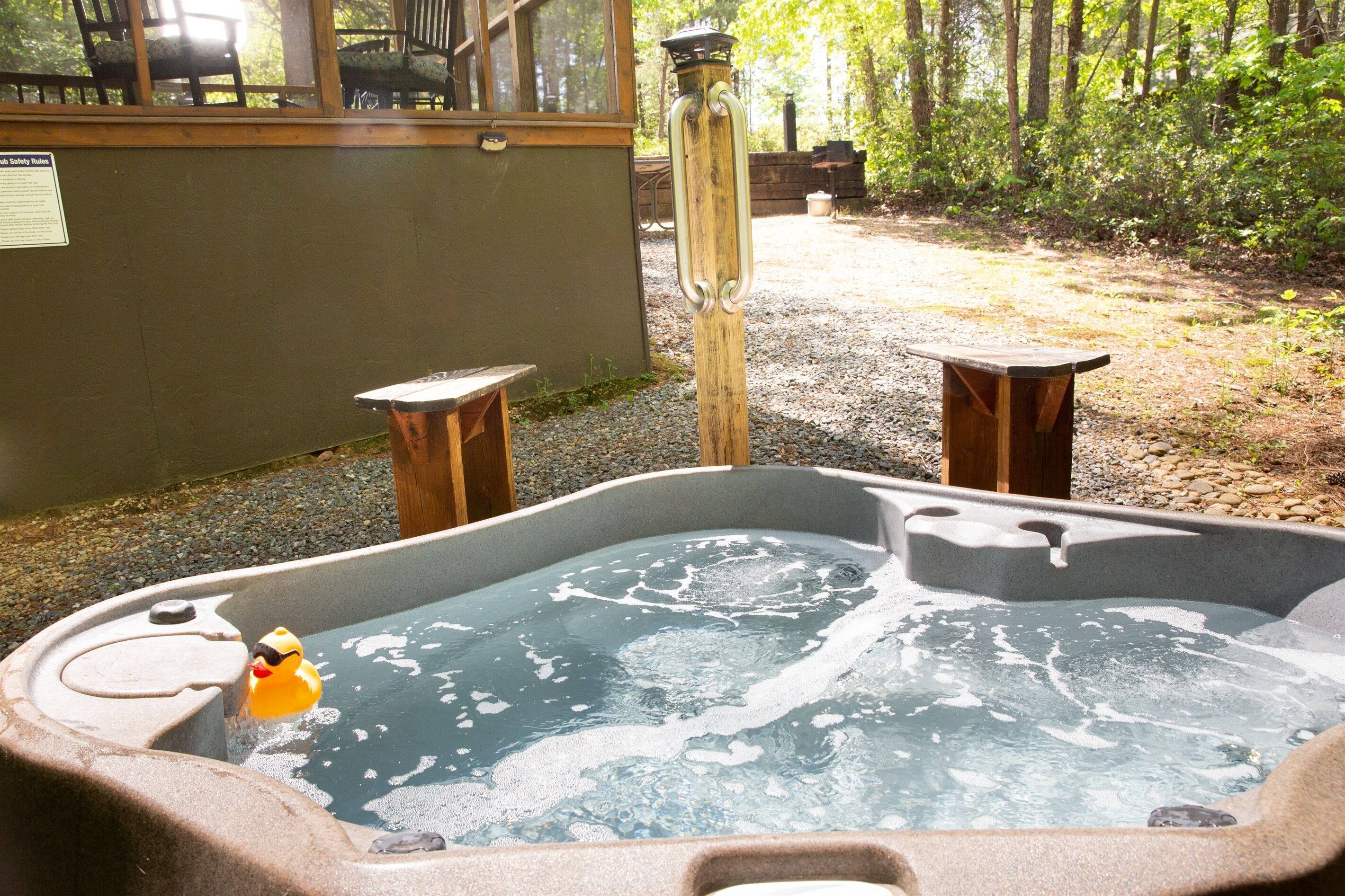 Un bain à remous avec un canard en plastique, entouré d’une terrasse en bois et bordé d’un chemin de gravier.