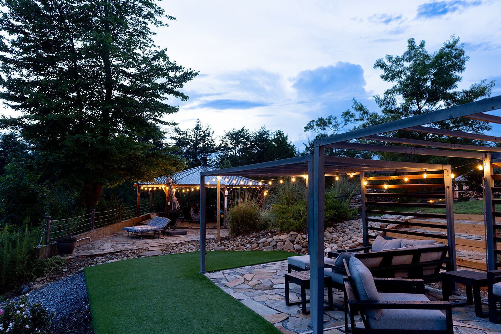 A covered outdoor patio area with stone flooring, a hammock, and string lights.