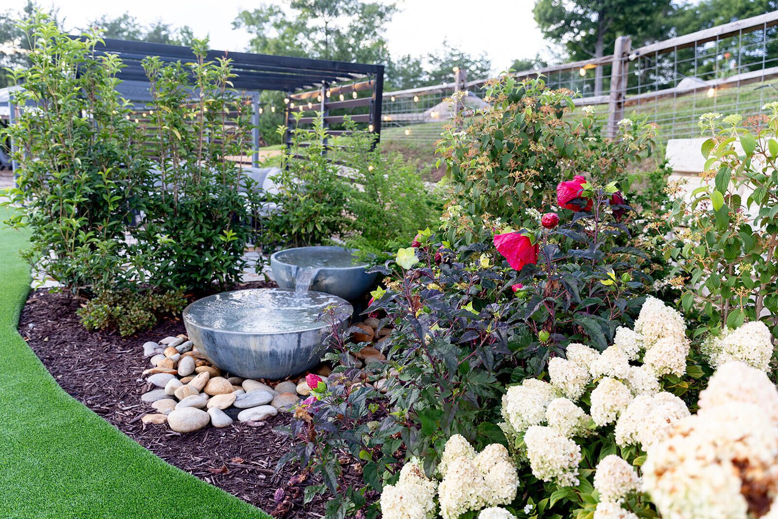 Un jardín con fuente de agua, rocas y diversas plantas.
