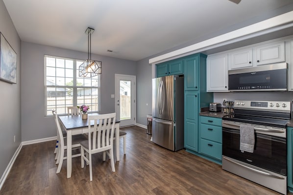 A modern kitchen with white cabinetry, a stainless steel refrigerator, a built-in oven, and a dining area with a wooden table and chairs.