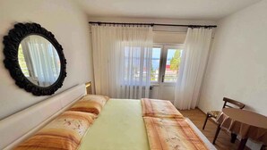 Une chambre à coucher comprenant un lit, une chaise, une table, un miroir et donnant sur l’extérieur.