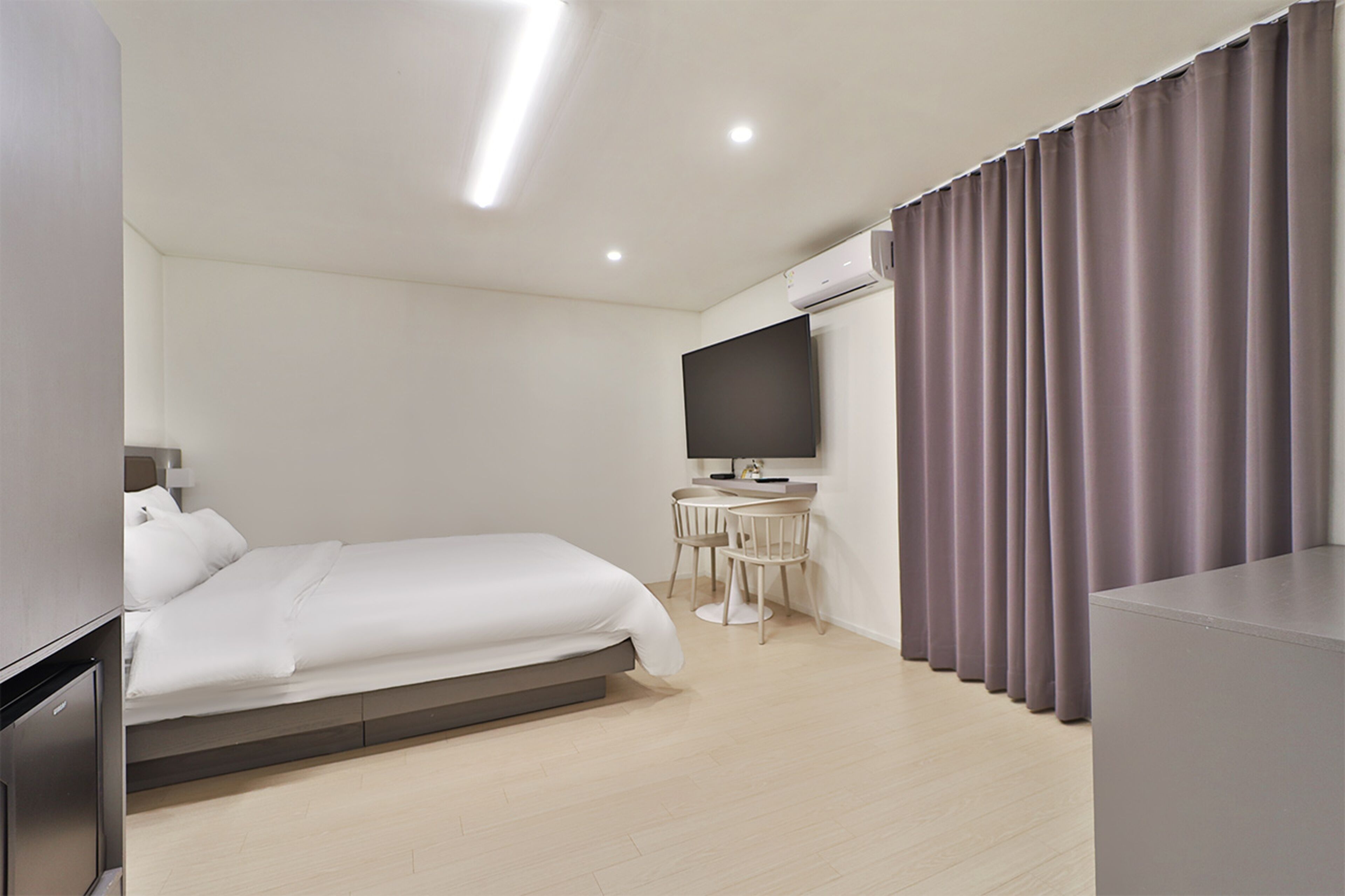 A modern hotel room with a bed, a desk, a flat-screen TV, and a large window with curtains.