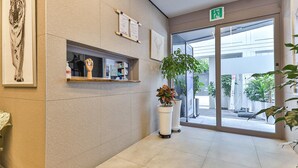 A reception area with a reception desk, framed artwork, potted plants, and a glass door leading outside. - Green B Hotel Busan Seomyeon (Busan)