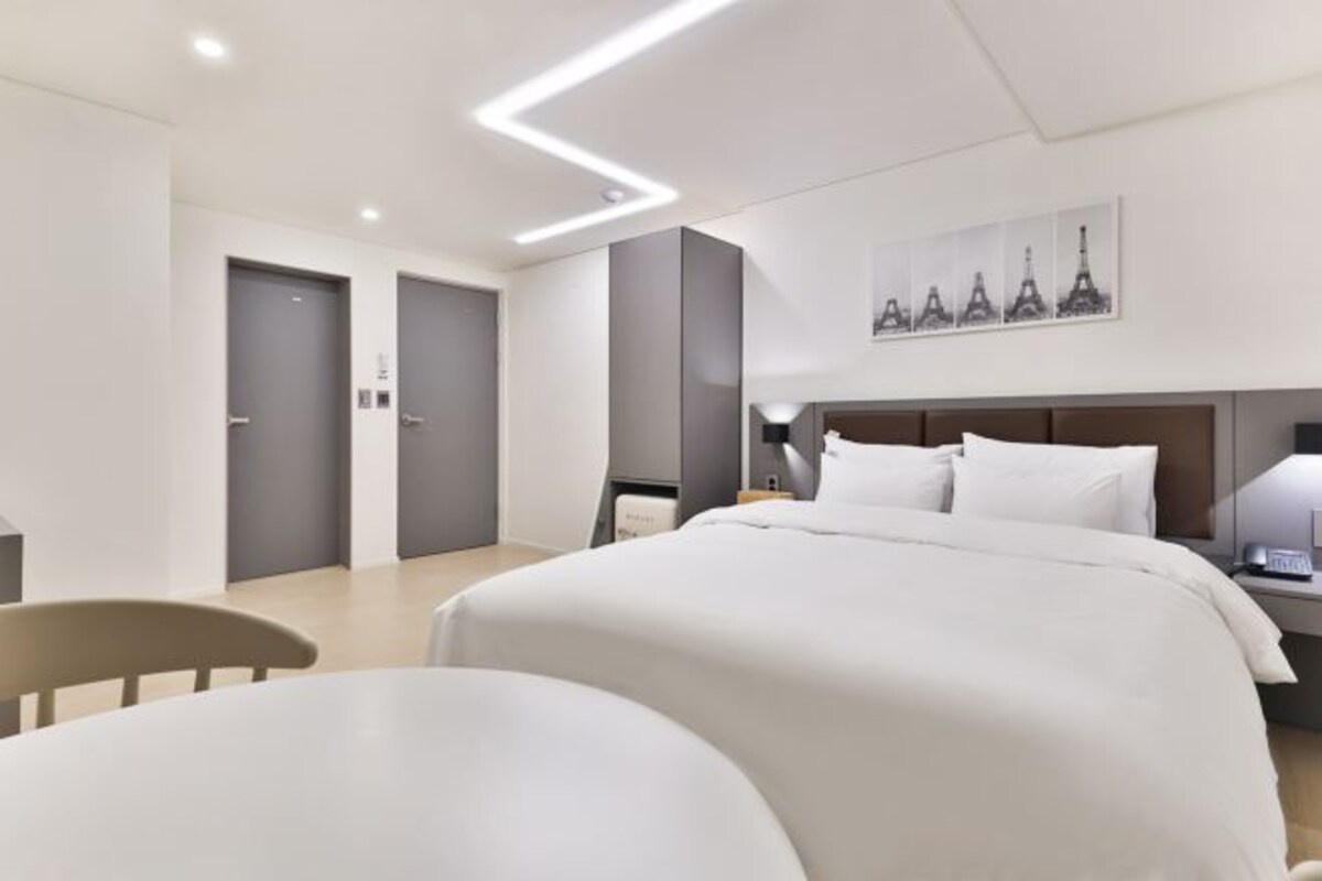 A modern hotel room with a large bed, a desk, and a chair. There is a painting of the Eiffel Tower on the wall.