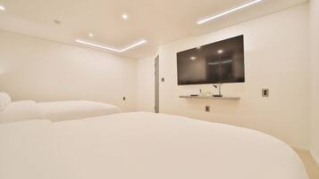 A modern bedroom with a large bed, a flat-screen TV mounted on the wall, and recessed ceiling lighting.