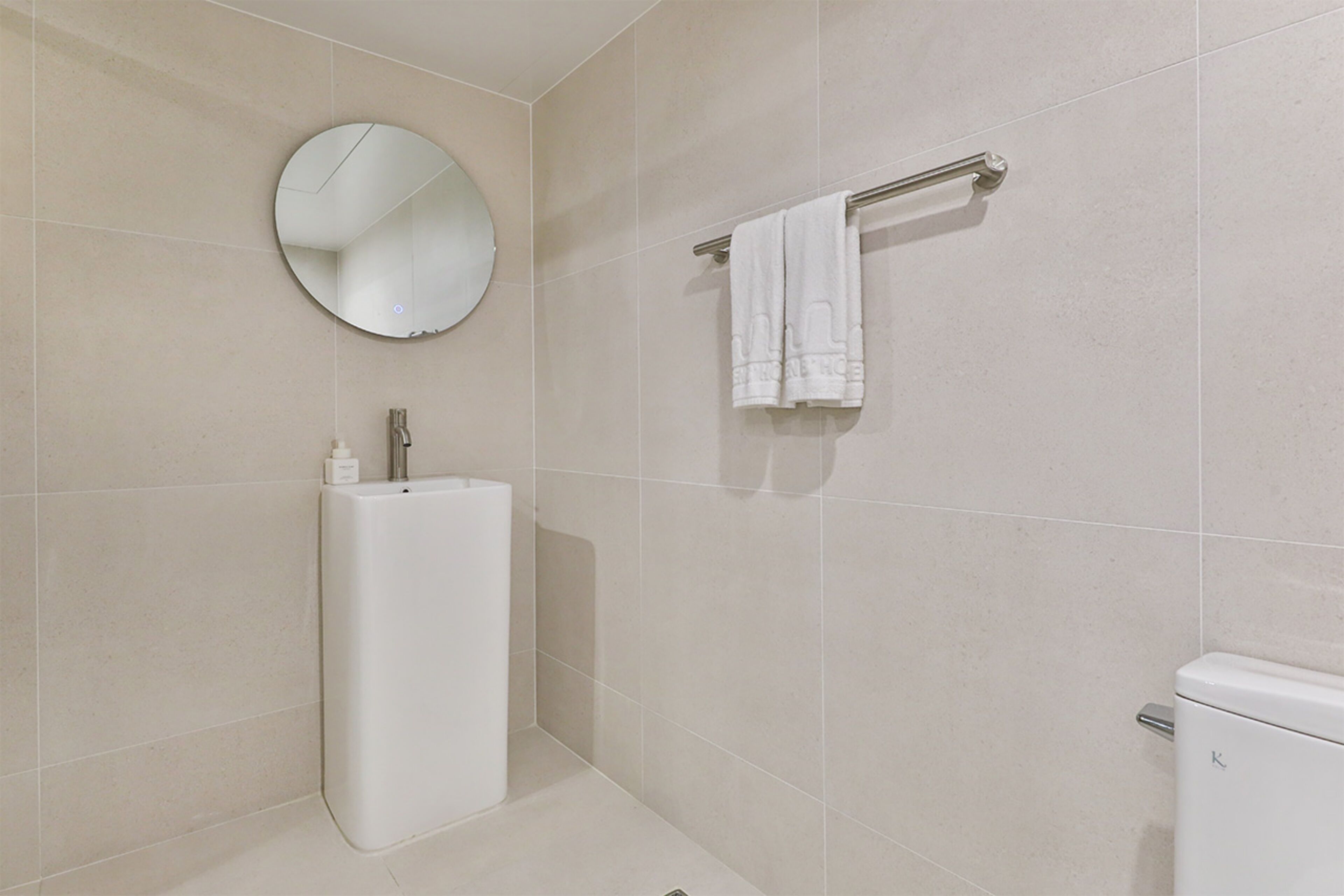 A modern bathroom with a round mirror, a towel rack with two towels, a white sink, and a toilet.