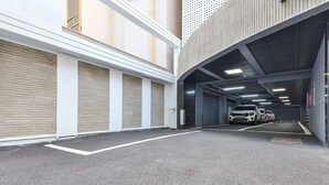 A multi-level parking garage with closed garage doors, a car in the distance, and a concrete ceiling with ventilation ducts. - Green B Hotel Busan Seomyeon (Busan)