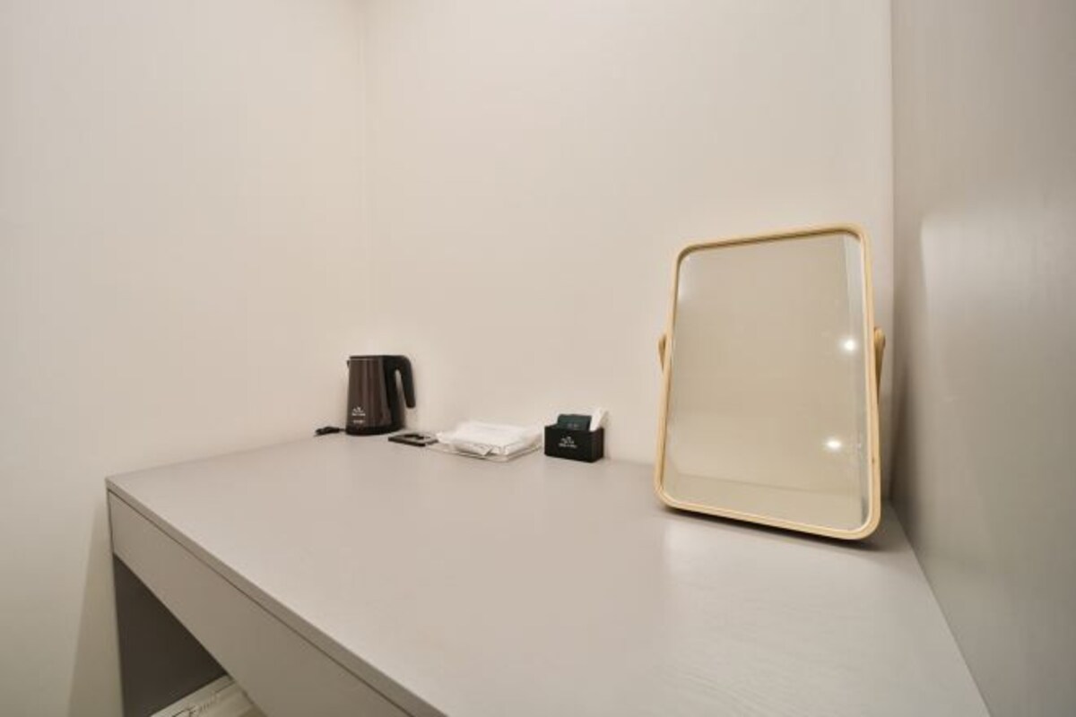 A hotel room with a white counter, a coffee maker, a tissue box, and a framed mirror.