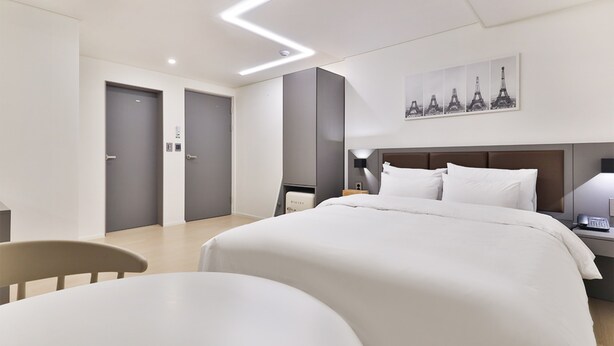 A modern hotel room with a large bed, a bedside table with a lamp, a chair, and a wall-mounted artwork of the Eiffel Tower. - Green B Hotel Busan Seomyeon (Busan)