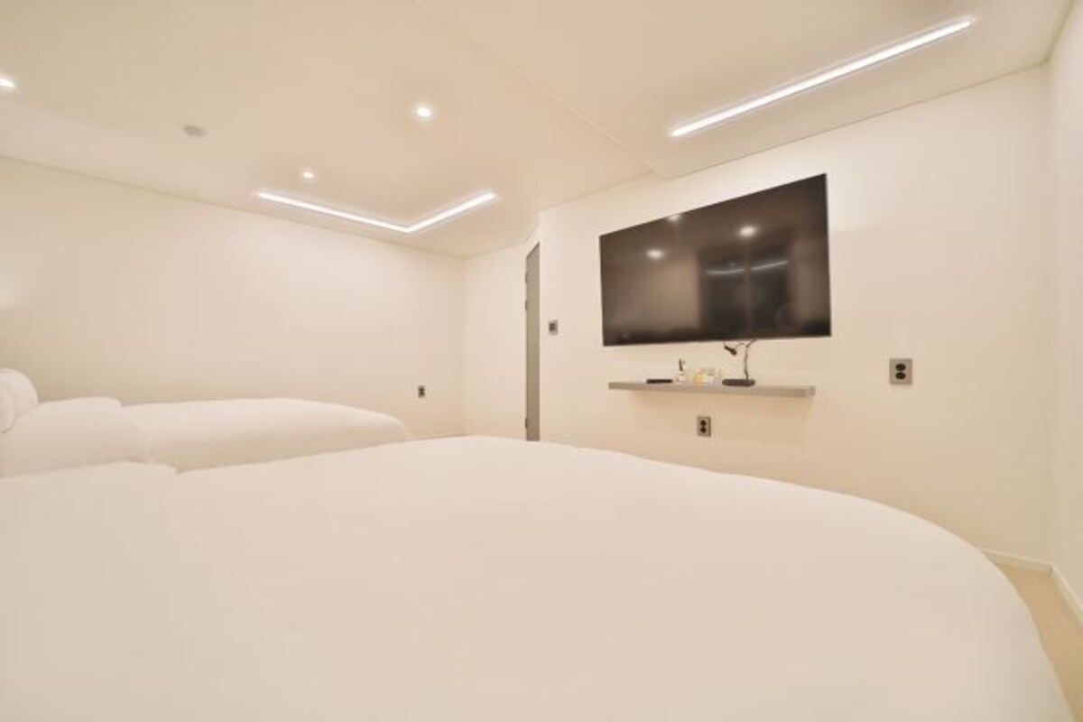 A modern hotel room with a large bed, a flat-screen TV mounted on the wall, and recessed ceiling lighting.