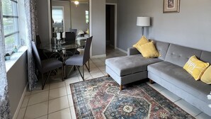 A living room with a gray sofa, a glass dining table, and a patterned rug. - 1bed apt in Hollywood&31st str. Independent apt with amazing backyard. (Hollywood)