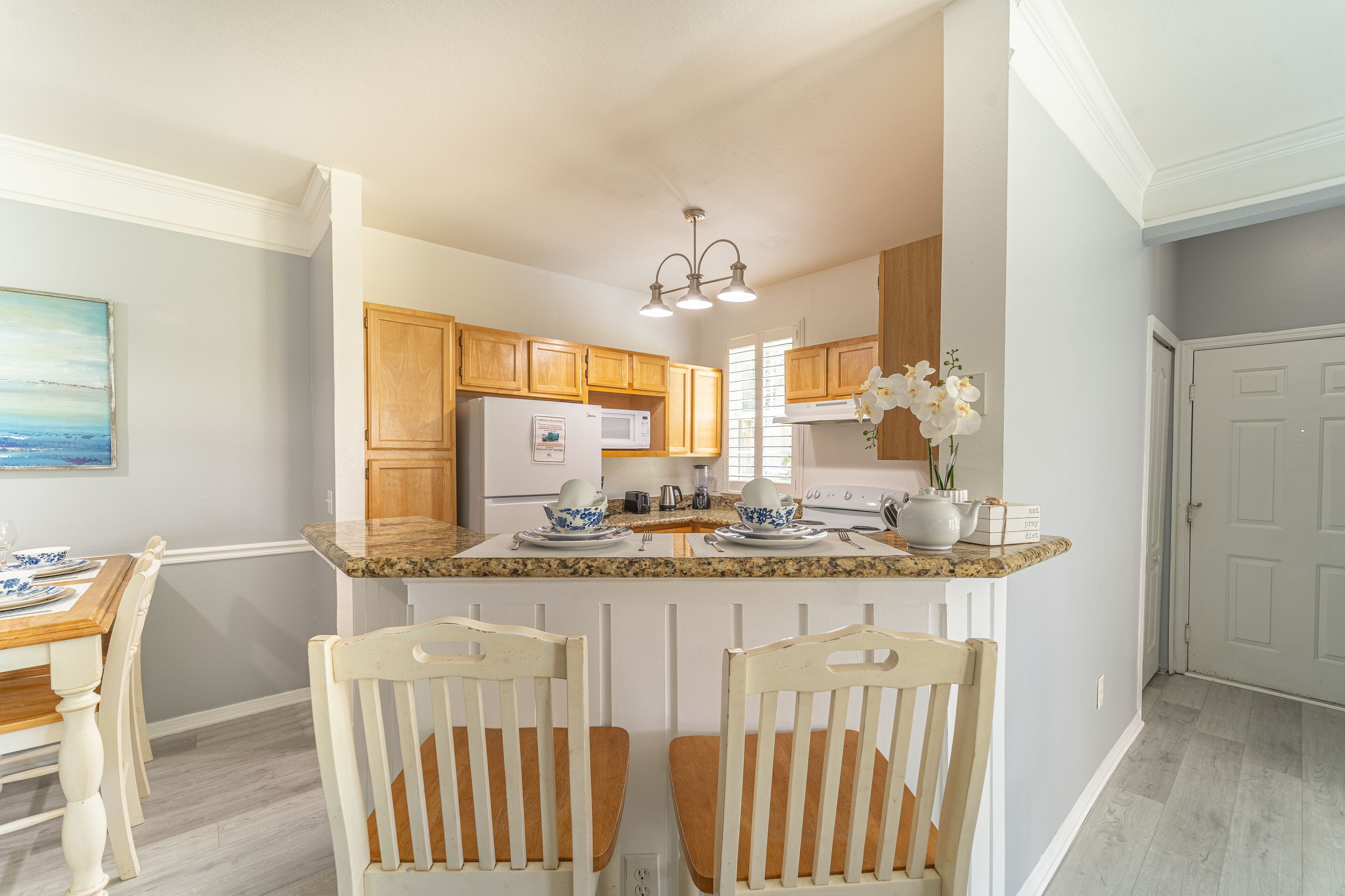 A kitchen with wooden cabinets, a granite countertop, and a dining area with two chairs and a table.
