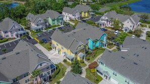 A residential area with multiple houses, a parking lot, and a body of water in the background.