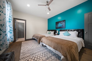 A hotel room with two beds, a ceiling fan, a teal accent wall, a patterned rug, and a door.