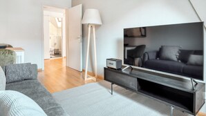 Una sala de estar moderna con un televisor de pantalla plana grande, un sofá gris, una lámpara de pie y una pequeña mesa con una radio.