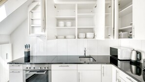 Una cocina moderna con armarios blancos, encimera negra, horno empotrado, microondas y hervidor.