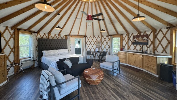A spacious tent with a large bed, a dining area, and a kitchen. - Glamping Yurt + Luxury Bath at Serenity Ridge (Mill Spring)