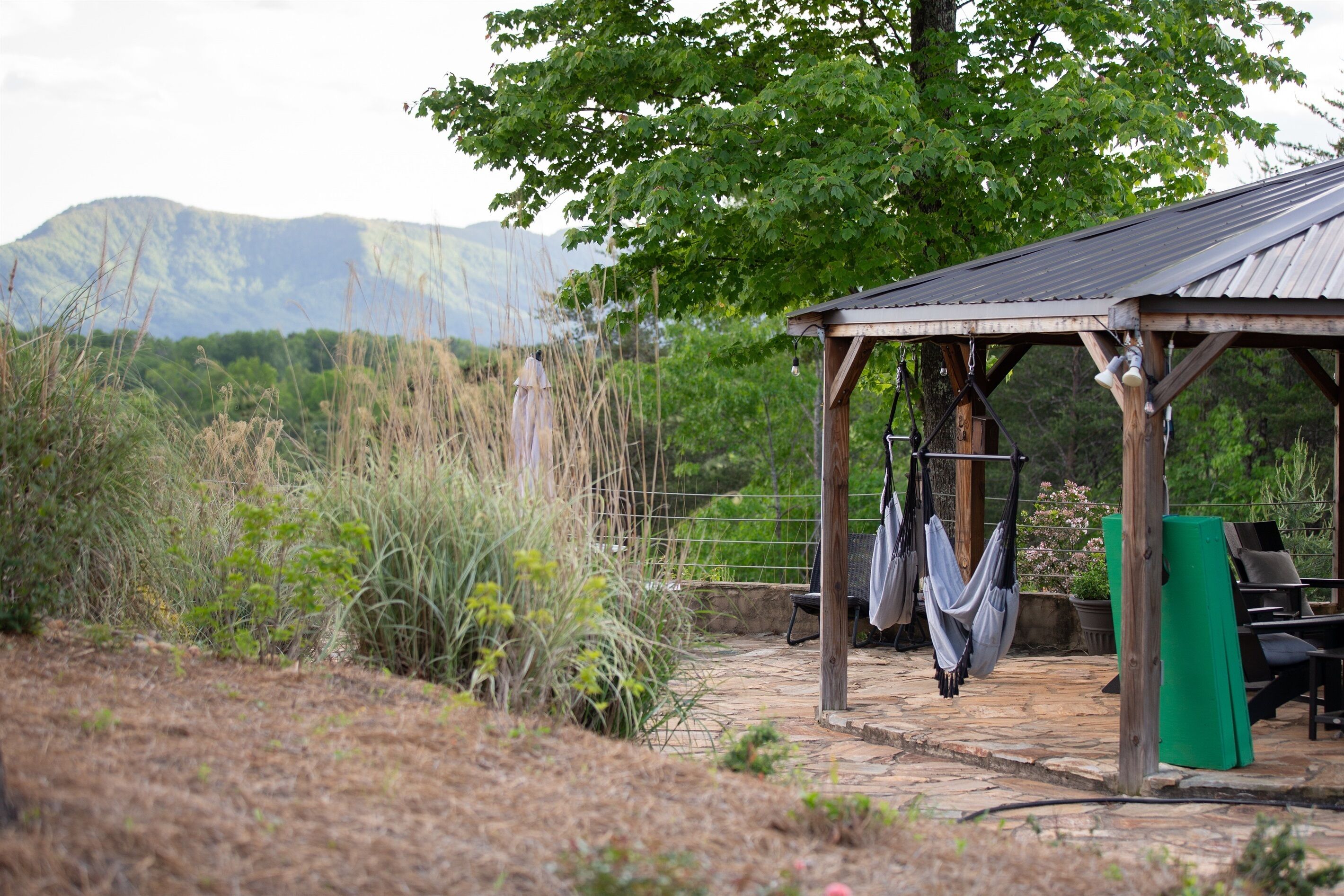 A rustic outdoor seating area with a wooden pergola, a stone pathway, and a view of mountains in the background.