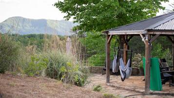 A rustic outdoor seating area with a wooden pergola, a stone pathway, and a view of mountains in the background.