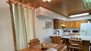 A wooden dining table with chairs, a kitchen area with wooden cabinets, a white refrigerator, and a ceiling light fixture. - Mountain Memory Cabin (Topton)