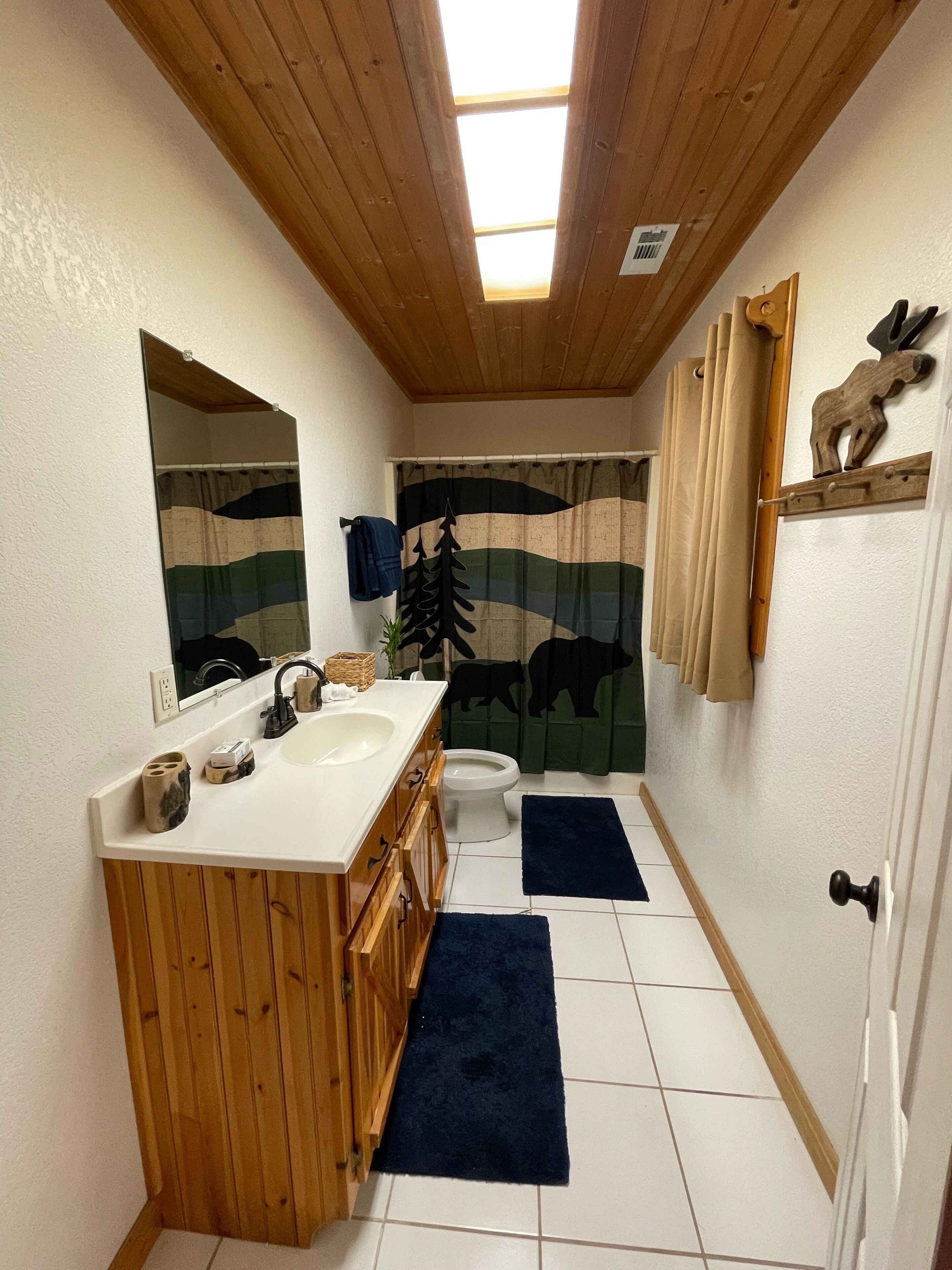 Un baño con tocador de madera, inodoro y cortina de ducha con diseño de bosque.