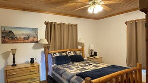 A bedroom with a wooden ceiling, a bed with a quilt, two bedside tables with lamps, a nightstand, a wooden dresser, and a painting on the wall. - Mountain Memory Cabin (Topton)