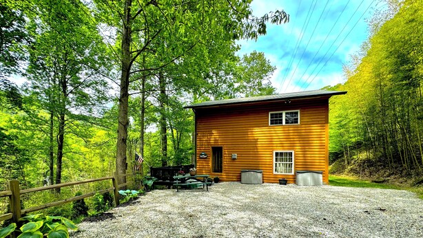 A wooden cabin with a gravel driveway, surrounded by dense forest. - Mountain Memory Cabin (Topton)