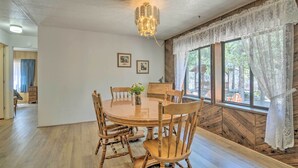 Un comedor con una mesa y sillas de madera, una araña y una ventana con cortinas de encaje.