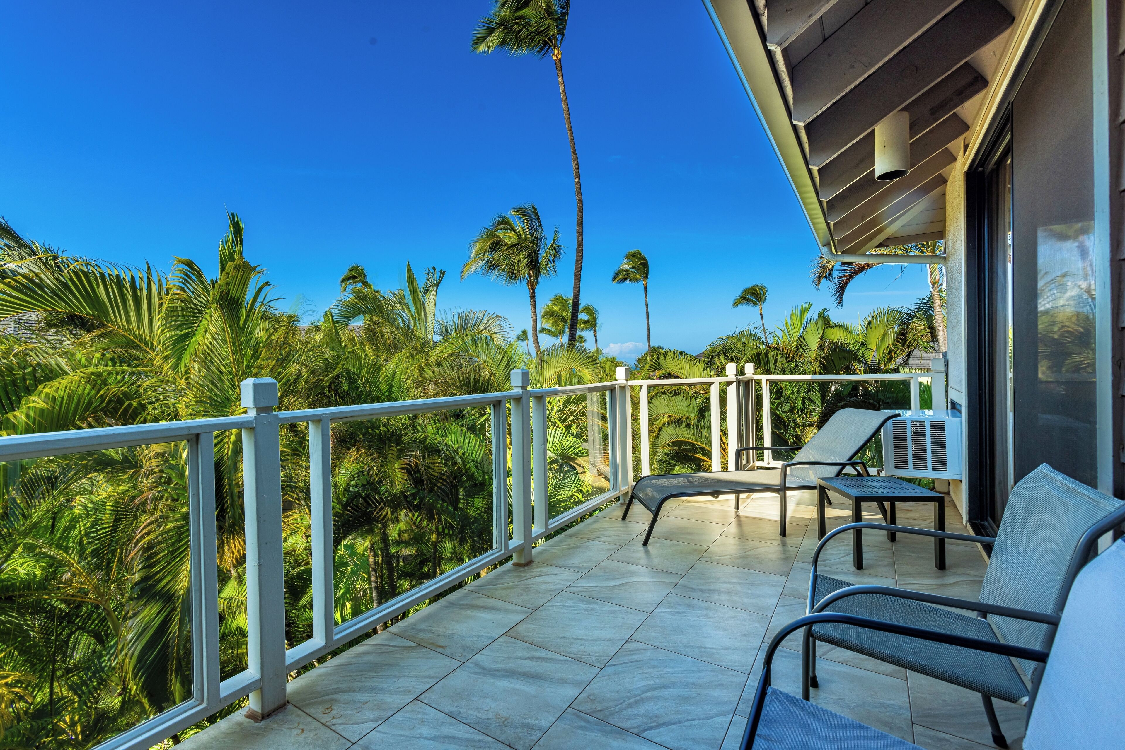 A balcony with a view of palm trees and a clear blue sky.
