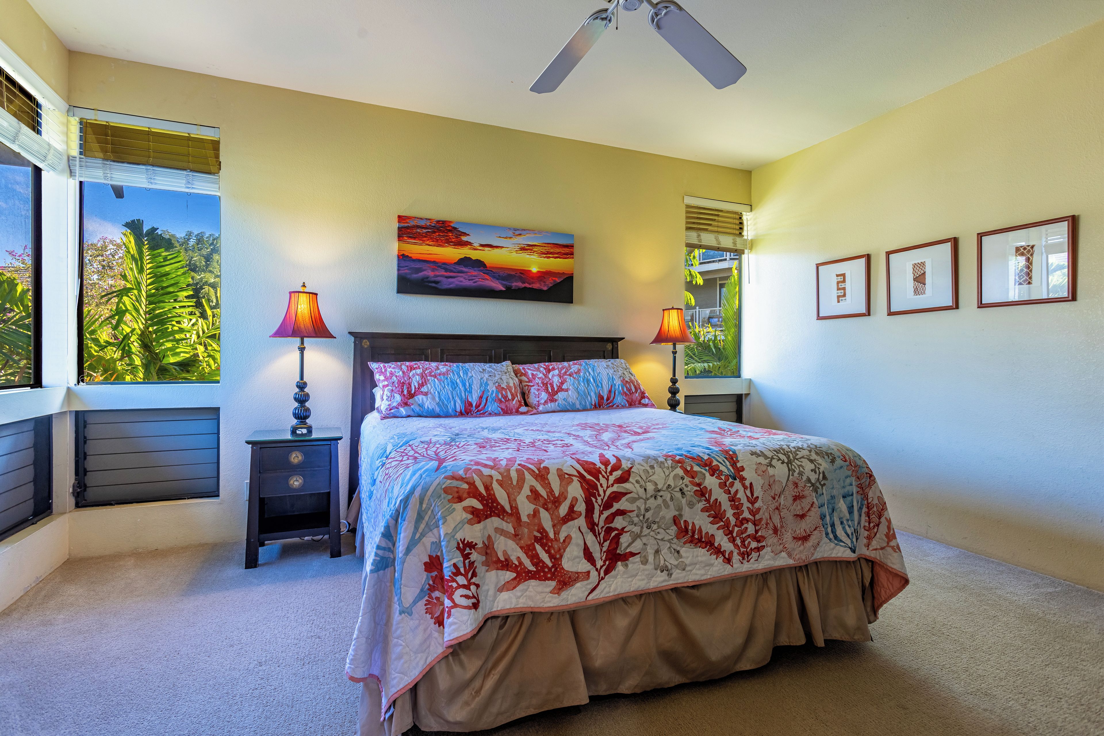 A bedroom with a large bed, two bedside tables, a ceiling fan, and a window with a view of greenery.