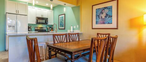 Un comedor con una mesa y sillas de madera, una cocina al fondo y una obra de arte enmarcada en la pared.