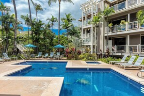 Un espace piscine avec des chaises longues, une piscine à l’eau d’un bleu limpide et un immeuble à plusieurs étages doté de balcons.