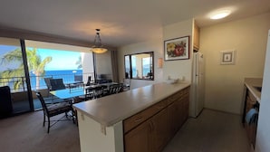 A kitchen with a large island, a dining area with a view of the ocean, and a refrigerator.