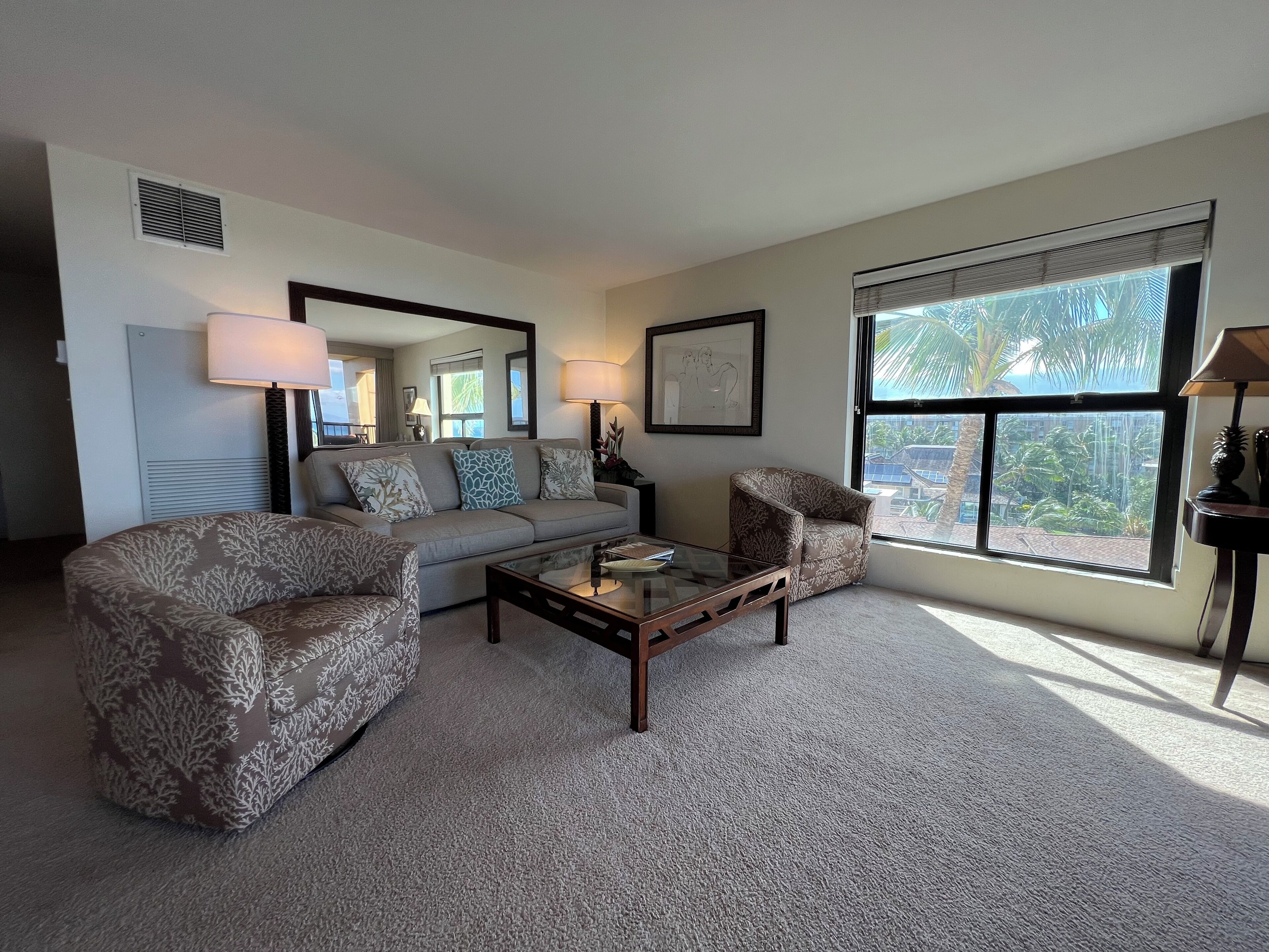 A living room with a sofa, armchairs, a coffee table, and a large window with a view of palm trees.
