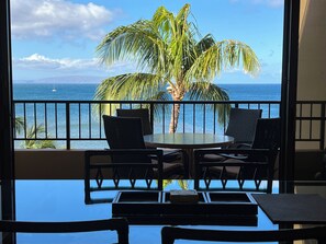Un balcon avec une table et des chaises, d’où l’on peut admirer un palmier et l’océan.