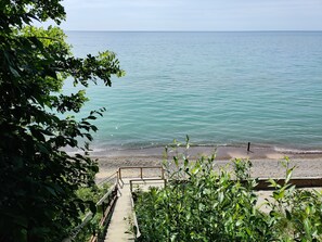 Un escalier en bois mène à une plage où l’eau est d’un bleu turquoise cristallin, et d’où l’on a une vue sur l’océan.