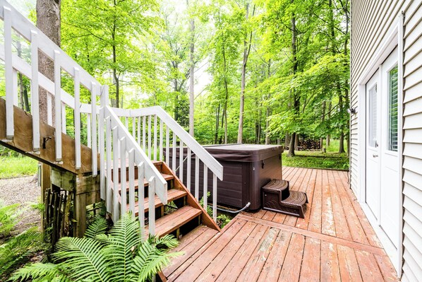 A wooden deck with a hot tub, a staircase, and a house in a forested area.