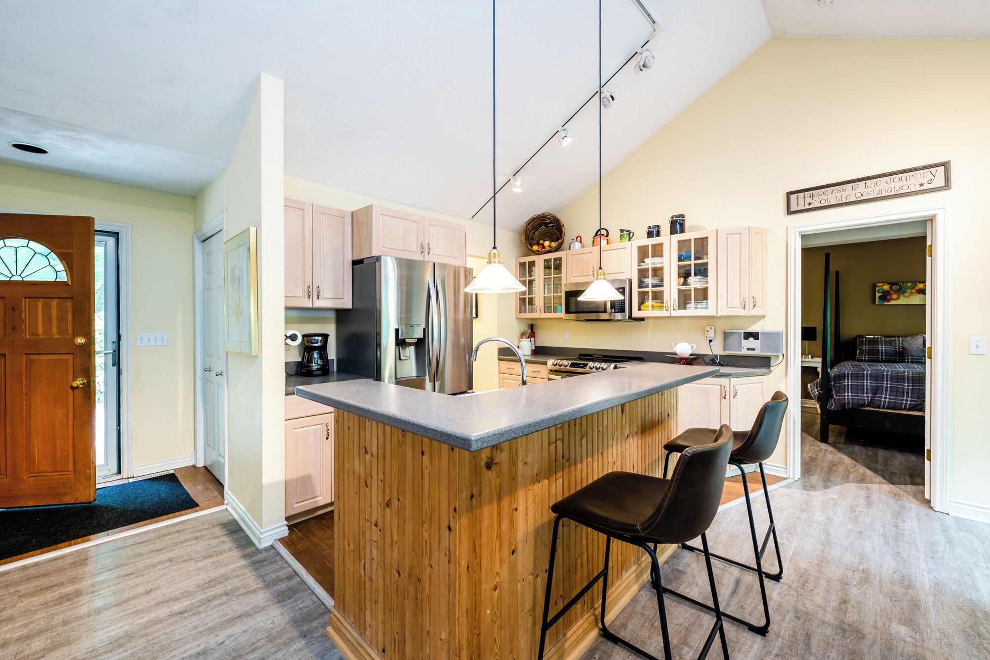 Une cuisine moderne avec des meubles en bois, des appareils électroménagers en acier inoxydable et un coin bar avec des tabourets.