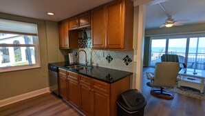 A kitchen with wooden cabinets, a black countertop, and a view of the ocean through large windows. - Beautiful direct ocean front beach access condo (Satellite Beach)