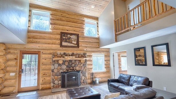 A log cabin interior with a stone fireplace, leather sofa, and a balcony.