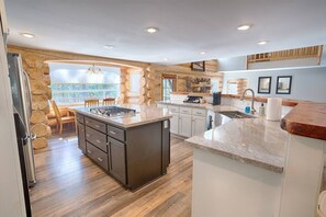 Une cuisine dotée d’un îlot central, d’un plancher en bois et d’un mur d’accent en pierre.