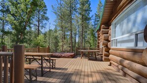 A log cabin with a deck, wooden benches, and tables.