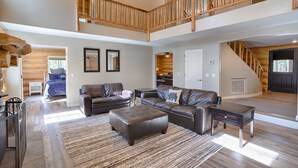 A spacious living area with a high ceiling, a wooden staircase, and a view of the outdoors.
